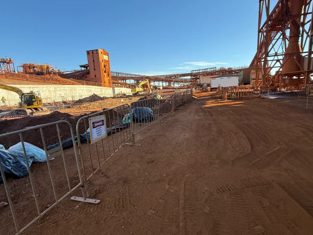 Two ANZ Enviro technicians in full PPE safely loading wrapped asbestos sheets into a skip bin at Mount Whaleback near Newman, WA